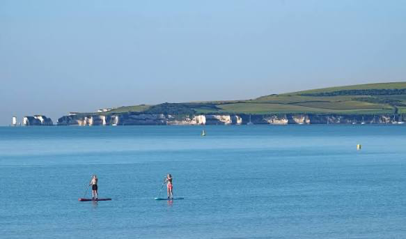 Paddleboarders on Poole Bay with Old Harry Rocks and the Dorset coastline beyond